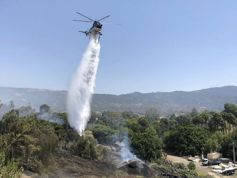 This Saturday, July 7, 2018, photo provided by the Santa Barbara County Fire Department shows a helicopter dropping water in concert with firefighters on the ground trying to extinguish stubborn smoldering areas of a fire in Goleta, Calif.